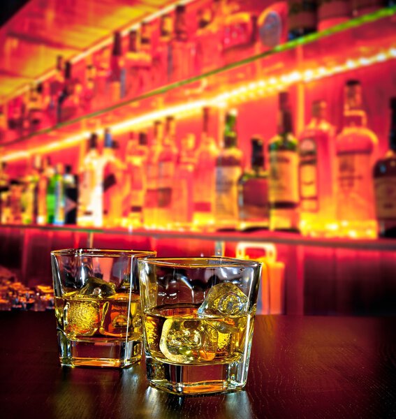 Стаканы виски со льдом на барном столе возле бутылки виски в теплой атмосфере
