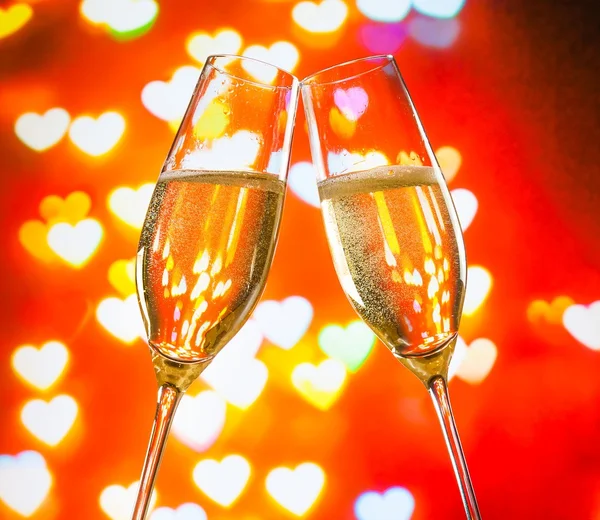 A pair of champagne flutes with golden bubbles on hearts bokeh background — Stock Photo, Image