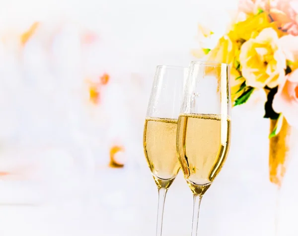 Champagne flutes with golden bubbles on wedding flowers background — Stock Photo, Image