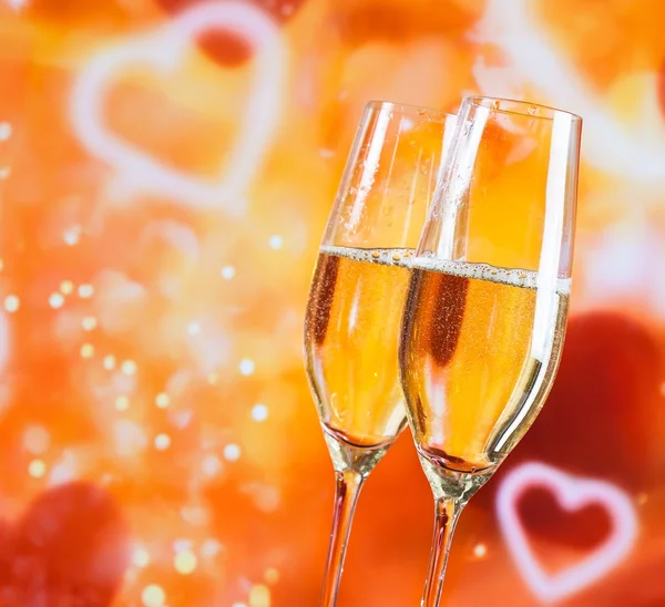 Флейты шампанского с золотыми пузырями на фоне размытых декоративных сердец — стоковое фото