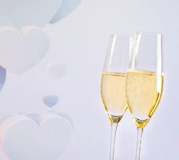 Champagne flutes with golden bubbles on blur decorative hearts background — Stock Photo, Image