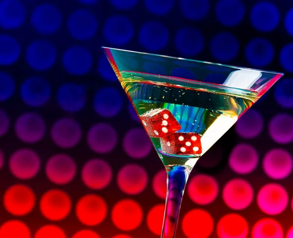 Red dice in the cocktail glass on colorful gradient bokeh — Stock Photo, Image