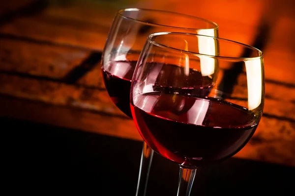 Dvě červené vinné sklenice na dřevěný stůl s příjemnou atmosféru na pozadí — Stock fotografie