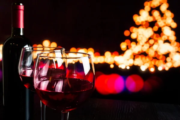 Red wine glass near bottle against bokeh lights background — Stock Photo, Image