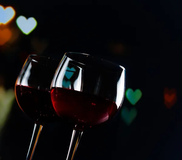 Two red wine glasses on hearts decoration bokeh lights background — Stock Photo, Image