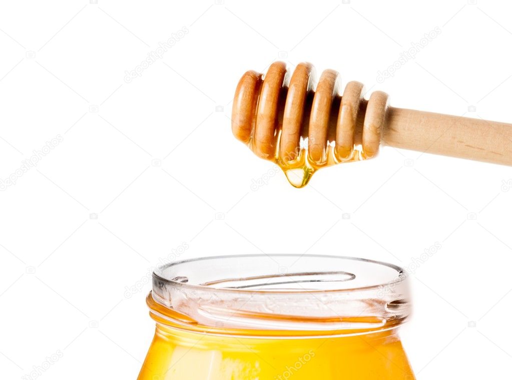 opened honey jar on white background with wooden honey dipper on top with drop honey