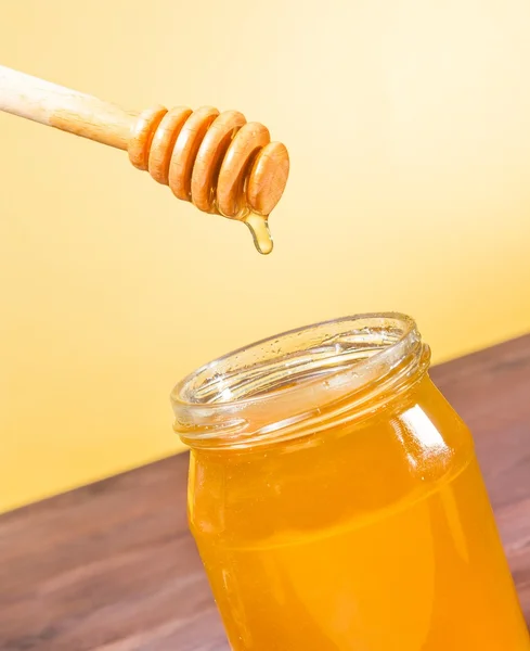 Honigglas auf Holztisch und goldenem Hintergrund mit hölzernem Honiglöffel oben mit Tropfenhonig — Stockfoto