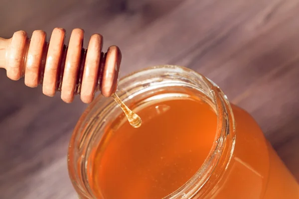 Honey jar on wood table with wooden dipper on top with drop honey — Stock Photo, Image