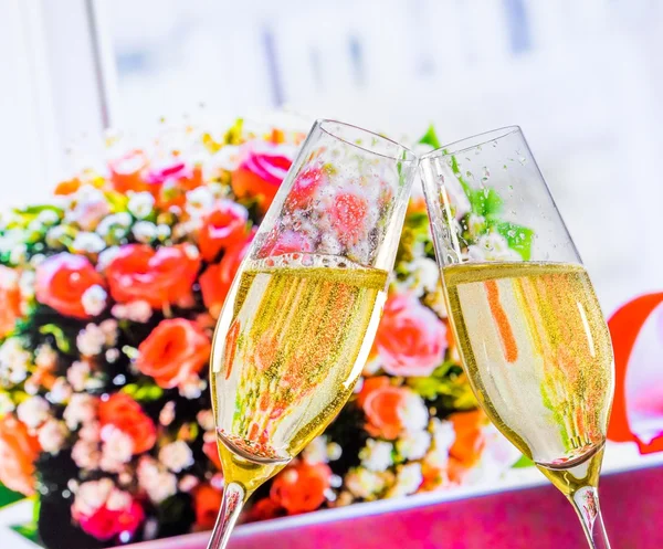 Champagne flutes with golden bubbles on wedding flowers background — Stock Photo, Image