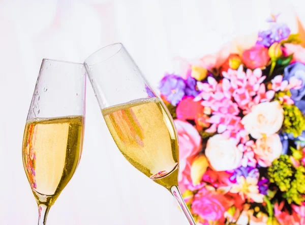 Champagne flutes with golden bubbles on wedding flowers background — Stock Photo, Image