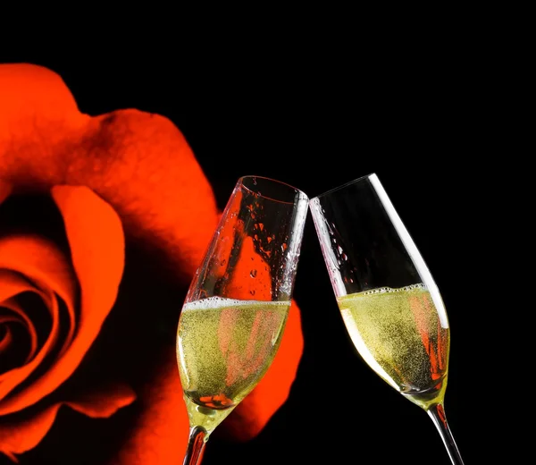 Champagne flutes with golden bubbles on rose flowers and black background — Stock Photo, Image