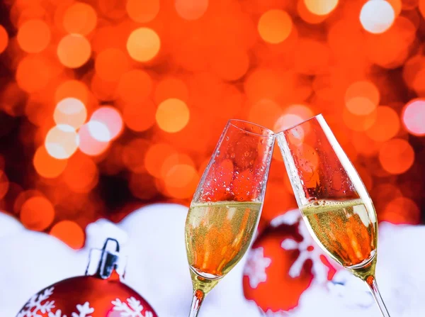 Champagne flutes with golden bubbles on red christmas lights bokeh and balls decoration background — Stock Photo, Image