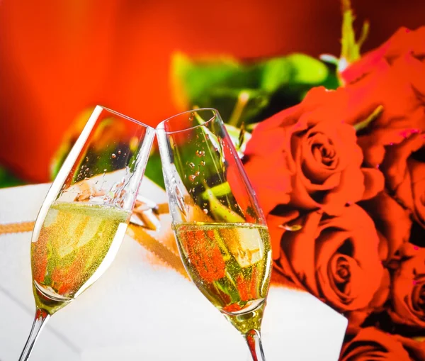 Champagne flutes with golden bubbles on wedding roses flowers background — Stock Photo, Image