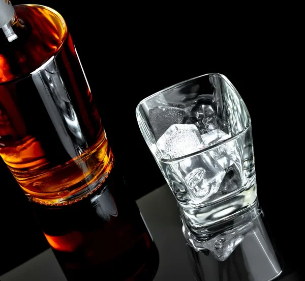 Top of view of empty whiskey glass with ice near bottle on black background — Stock Photo, Image