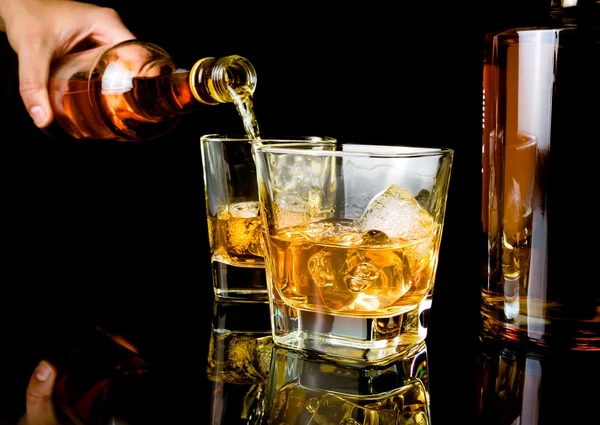 Barman derramando uísque na frente de vidro de uísque e garrafas — Fotografia de Stock