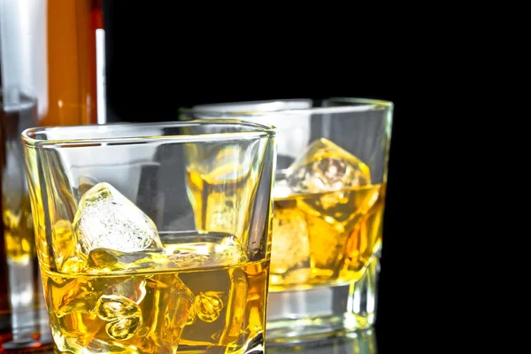 Whiskey with ice in glasses near bottle on black background — Stock Photo, Image