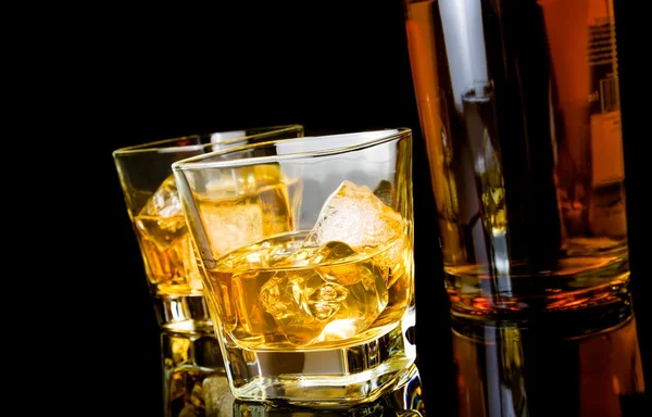 Whisky s ledem v brýlích poblíž láhev na černém pozadí — Stock fotografie