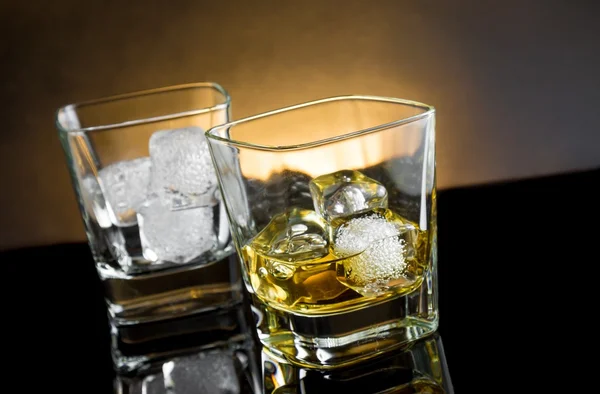 Whiskey glasses with ice and warm light on black background — Stock Photo, Image