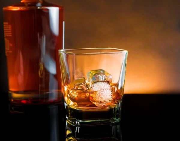 Whiskey glass with ice and warm light on black table, warm atmosphere — Stock Photo, Image