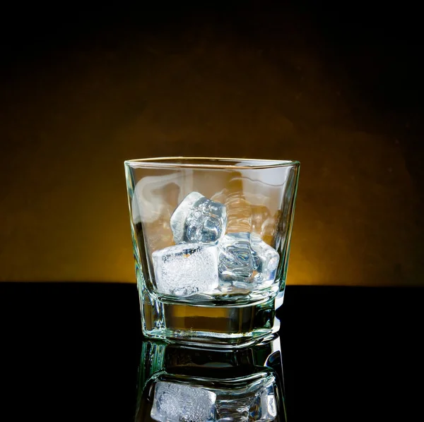 Copo de uísque vazio com gelo e luz quente na mesa preta — Fotografia de Stock