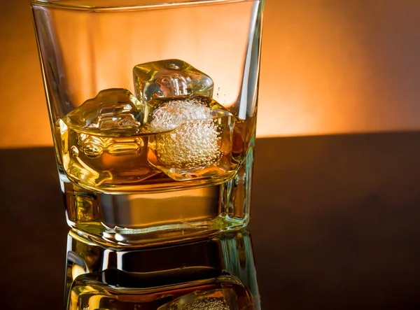 Whiskey glass with ice and warm light black table, warm atmosphere — Stock Photo, Image