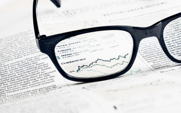 Finanční diagram a graf měny vidět skrz brýle čočky na finanční noviny — Stock fotografie