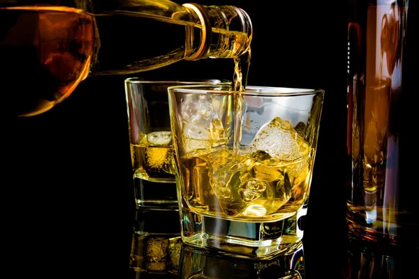 Barman vertiendo whisky frente al vaso de whisky y las botellas — Foto de Stock