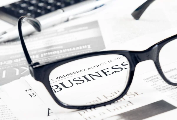 Business word see through glasses lens on financial newspaper near calculator — Stock Photo, Image