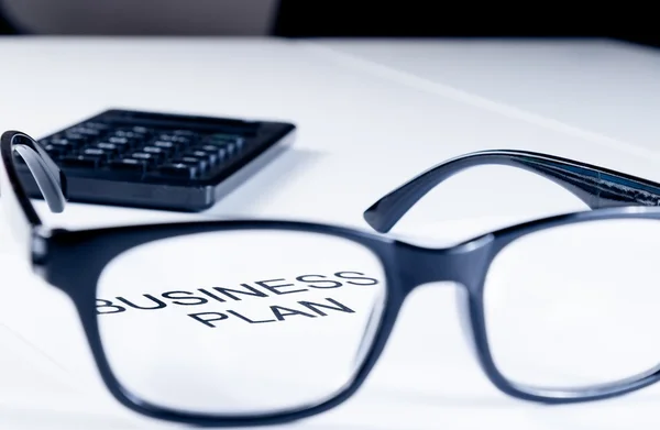 Business plan words see through glasses lens near calculator, business concept — Stock Photo, Image