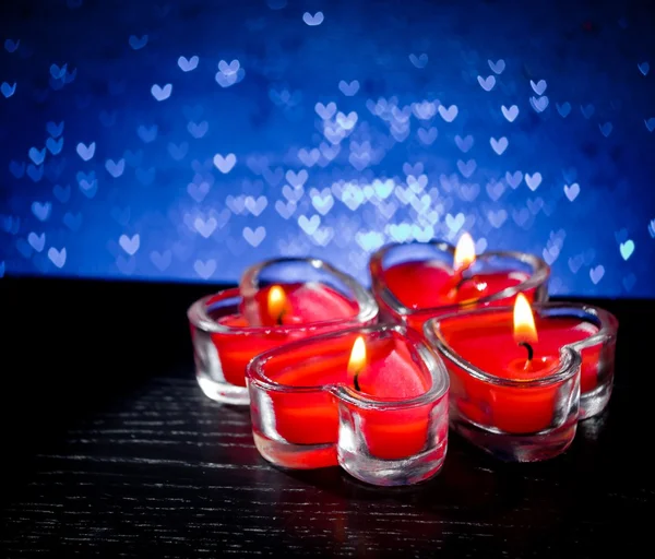 Red burning heart shaped candles on blue hearts bokeh — Stock Photo, Image