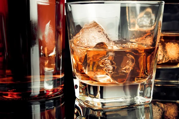 Whisky s ledem ve skle na černém pozadí poblíž láhev — Stock fotografie