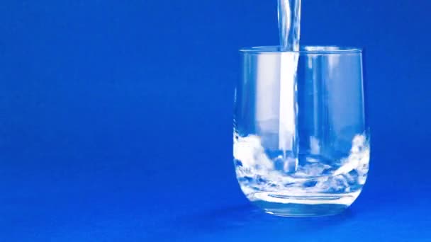 Vyplňování sklenici s vodou na modrém pozadí