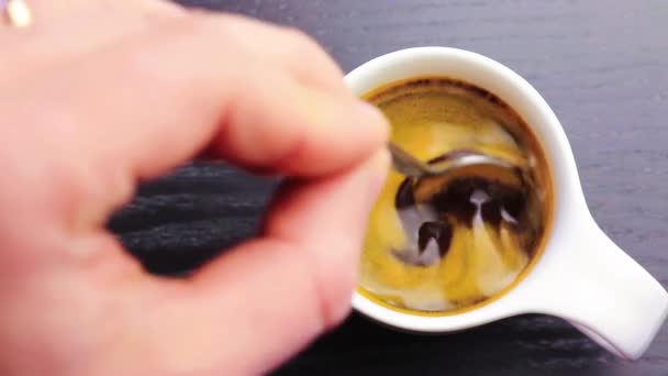 Tazza di caffè con mano adulta che usa un cucchiaio all'interno, sul tavolo in legno nero — Video Stock