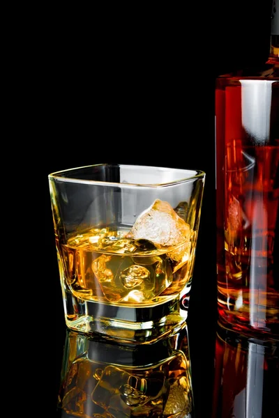 Whiskey con hielo en vidrio cerca de la botella sobre fondo negro —  Fotos de Stock
