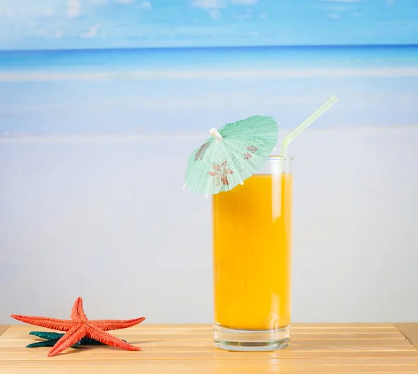 Szklanka soku pomarańczowego na morza i piaszczystej plaży w pobliżu rozgwiazda — Zdjęcie stockowe