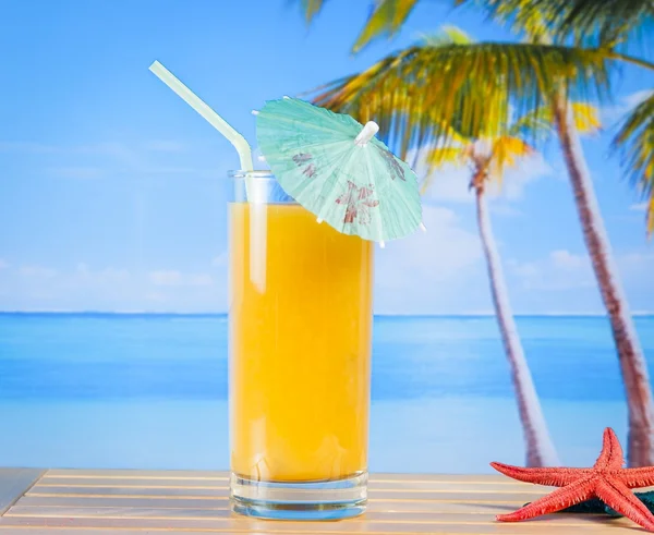 Szklanka soku pomarańczowego na piaszczystej plaży w pobliżu rozgwiazda — Zdjęcie stockowe