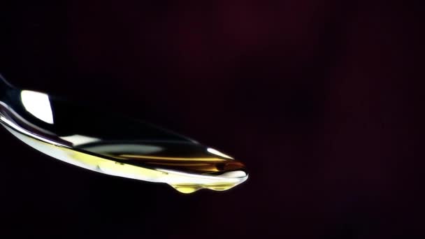 Aceite de oliva virgen extra sobre una cuchara con gotas aisladas sobre fondo de madera oscura — Vídeo de stock