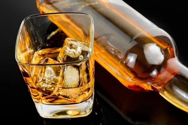 Górnej części widoku kieliszek whisky w pobliżu butelka czarny tabela z odbiciem — Zdjęcie stockowe