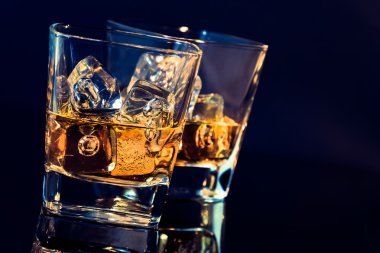 iki bardak viski ile hafif renk tonu mavi siyah arka plan üzerine buz küpleri ile