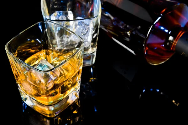 Top of view of glass of whiskey near bottle on black table with reflection — Stock Photo, Image