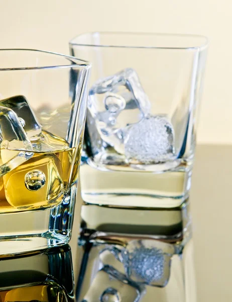 One glass of whiskey and one empty with ice cubes on table with reflection — Stock Photo, Image