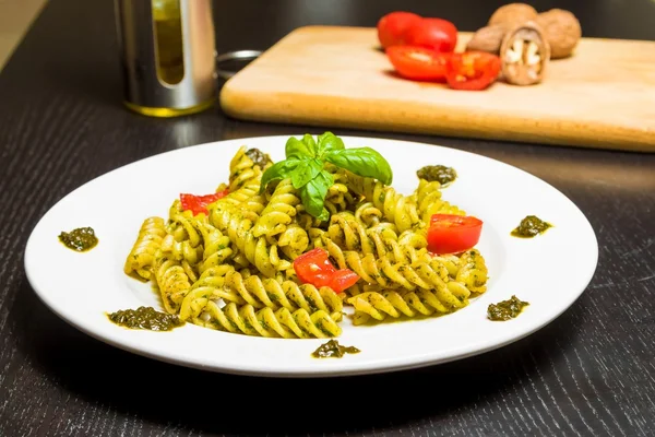 Dish of pasta with pesto genovese sauce and vegetables, tomato and basil on black wood table — Stock Photo, Image