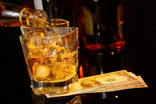 Barman versando whisky davanti a bicchiere di whisky e bottiglie vicino dollari Immagini Stock Royalty Free