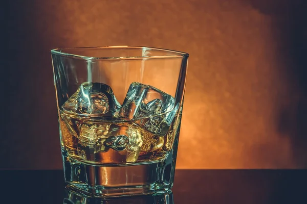 Vaso de whisky sobre mesa negra con reflejo, ambiente cálido — Foto de Stock