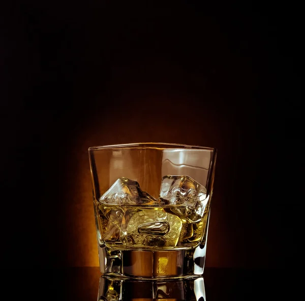 Glass of whiskey on black table with reflection, warm atmosphere — Stock Photo, Image