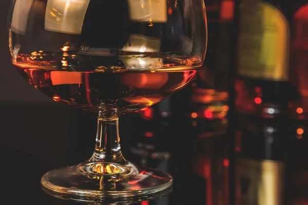 Snifter di brandy in elegante bicchiere di cognac tipico davanti alle bottiglie in sottofondo — Foto Stock