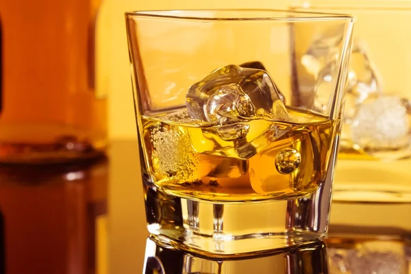 Primer plano de dos vasos de whisky cerca de la botella en la mesa con reflexión, ambiente cálido — Foto de Stock