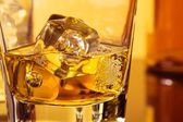 detail sklenici whisky s ices poblíž láhev na stůl s odleskem, vřelou atmosféru