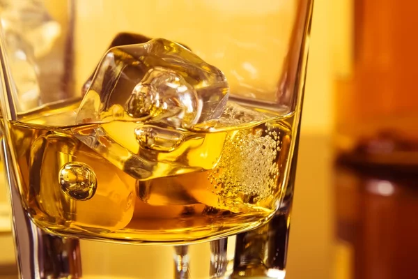 Detalj av glas whiskey med ices nära flaskan på bordet med reflektion, varm atmosfär — Stockfoto