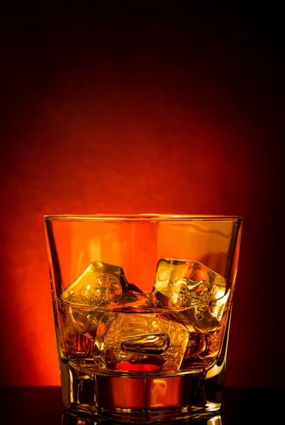 Sklenici whisky na černý stůl s odraz, červený nádech atmosféry — Stock fotografie